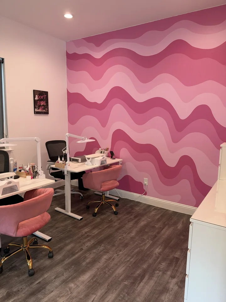 Manicure tables and pink client chairs beside the pink wave wall at YA Studio